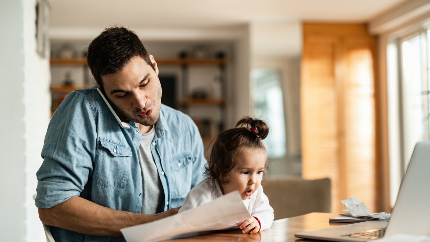 A father reviewing documents at home while holding his daughter