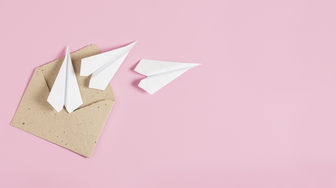 Aviones de papel saliendo de un sobre sobre un fondo rosa